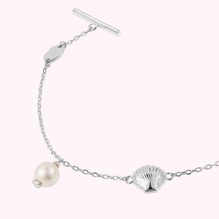 Close up image of a sterling silver bracelet with shell and freshwater pearl charms and lip shaped links.