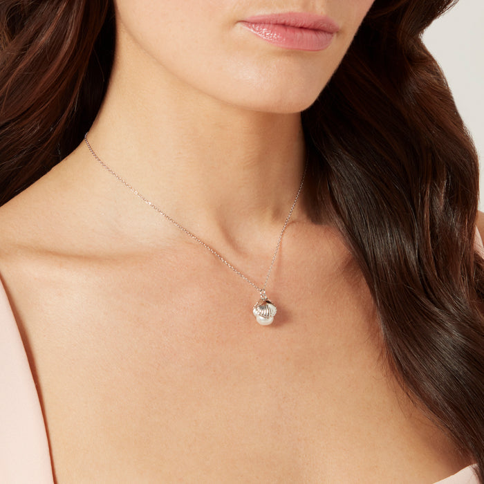 Model with dark hair wearing a sterling silver shell shaped pendant with a freshwater pearl.