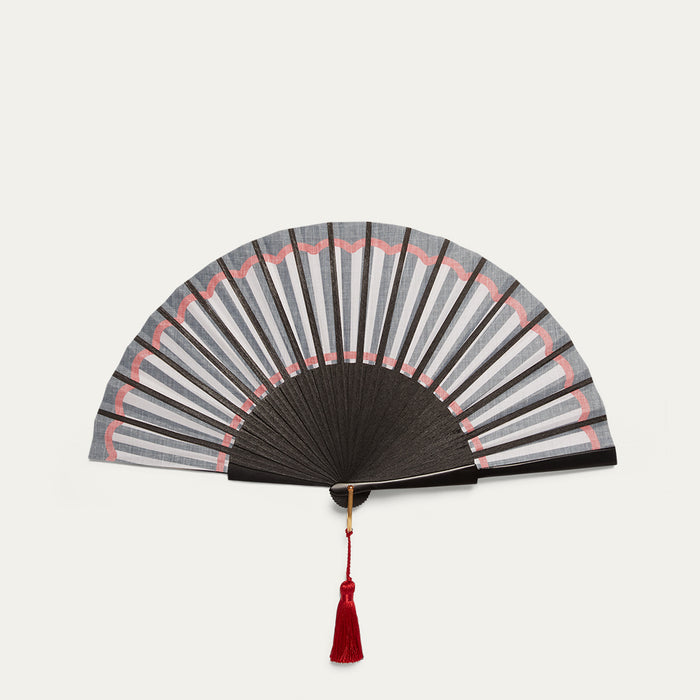 Black and white hand fan with a red tassel on a light gray background