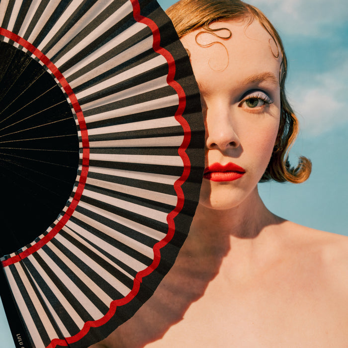 Woman holding a black and white striped fan with red accents against a blue sky.