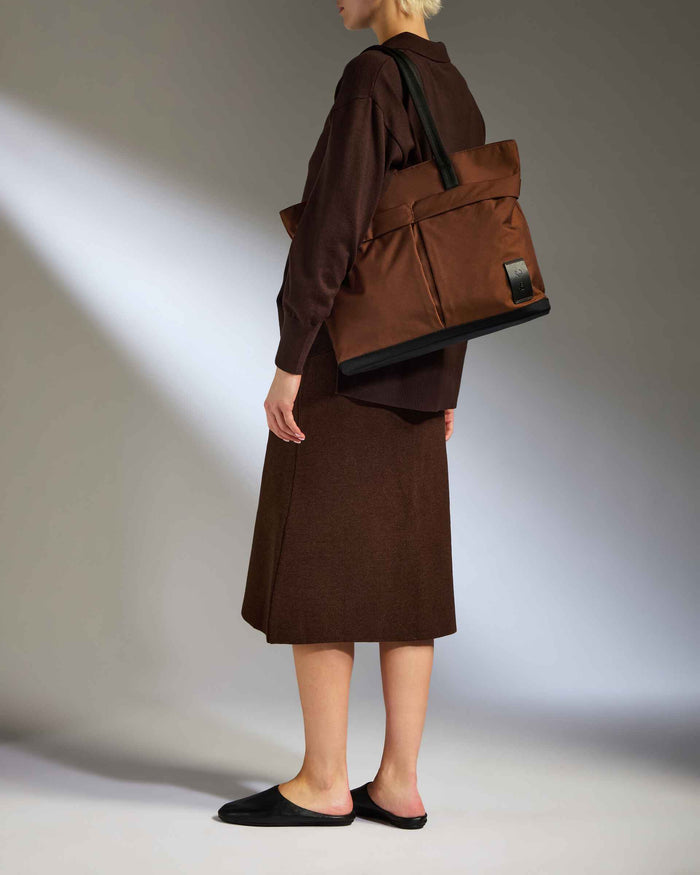 a woman in brown skirt and brown jacket holding a brown bag