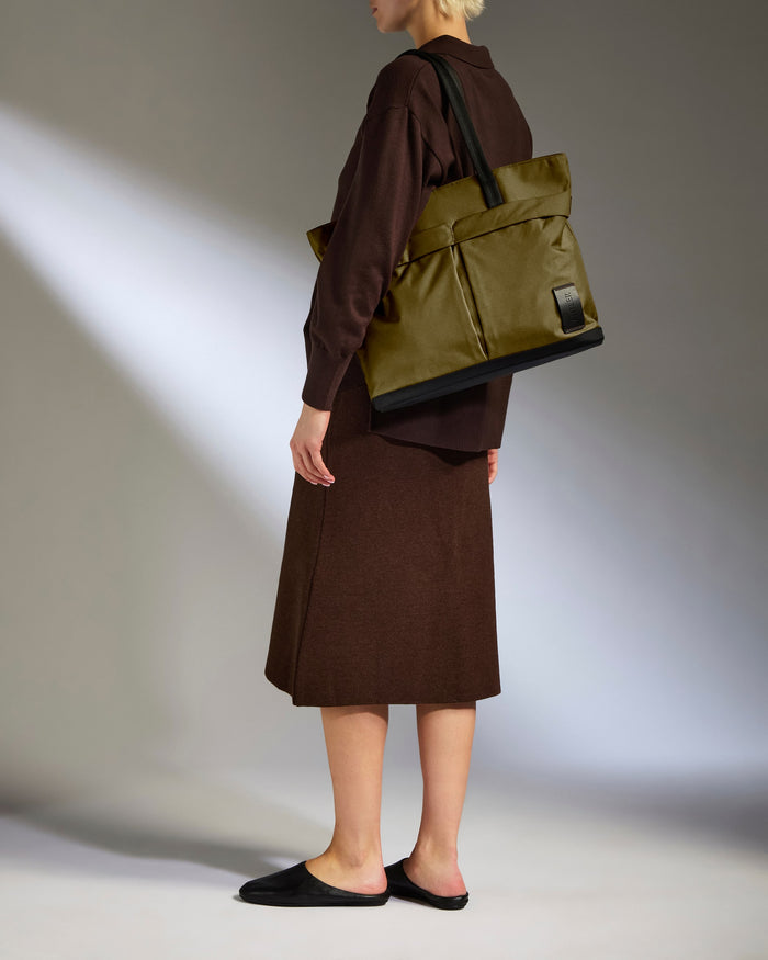 a woman in brown dress and brown jacket holding a green bag