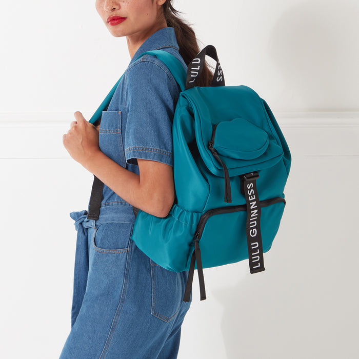 Woman wearing teal Lulu Guinness backpack against white background.
