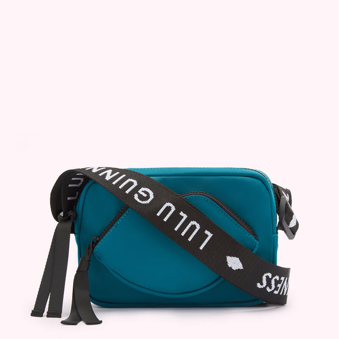 Teal Lulu Guinness crossbody bag with a lip-shaped front pocket and black strap with white logo.