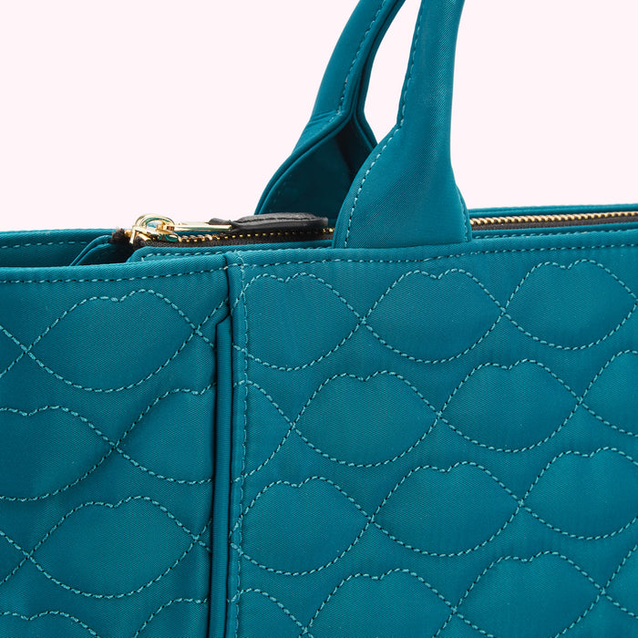 Close-up of a teal quilted tote bag with gold zipper and black handles.