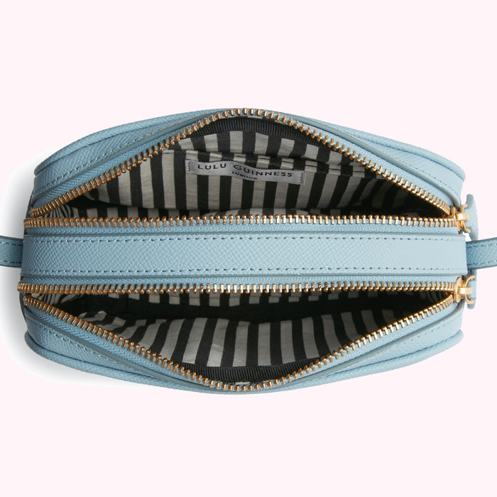 Overhead view of a pale blue Lulu Guinness London crossbody bag open to reveal its black and white striped interior lining.