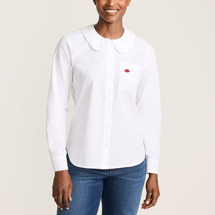 Women wearing a white cotton shirt with a round peter pan collar and red embroidered lip on the pocket against a beige background