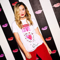Image of celebrity Laura Whitmore standing in front of a black and white stiped background wearing a Choose Love with Lulu Guinness charity t-shirt.