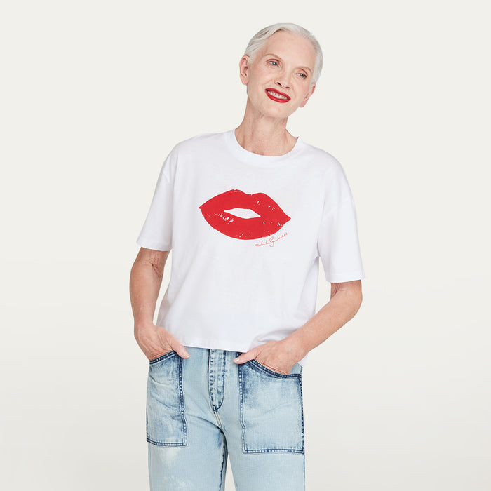 Person wearing a white t-shirt with a red lip print design on a plain background