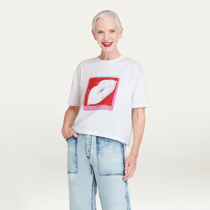 Person wearing a white t-shirt with a graphic lip design and light blue jeans on a plain background
